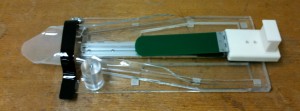 Figure 1: The Time Card Packaging System: the client slides the bag onto the funnel on the left side, and places the papers on the loading platform in the middle. The green acrylic flap is on a hinge, and the client flips it town on top of the papers before sliding them into the bag.